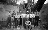 Män med spadar och skyfflar framför en grävmaskin, i Jönköping.