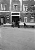 Tre män står utanför Centralhotellet i Jönköping. Bredvid ligger en frukt- och konfektyraffär.