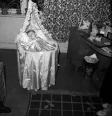 Bäck. Ett litet barn iförd dopklänning ligger i en babykorg med sänghimmel i en lägenhet i Jönköping.