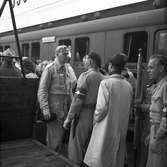 På perrongen står resenärer bredvid ett tåg till Stockholm C. Två uniformsklädda män samtalar med varandra.