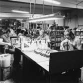 Män arbetar vid olika maskiner för skotillverkning. En stor del av produktionen består av träskor med namnet Dalbo.   Holm.Se hembygden 1972, s. 156