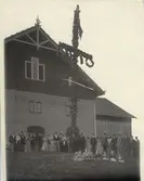 Midsommar. Kilanda  Barn, kvinnor och män är palcerade vid ett midsommarstång.