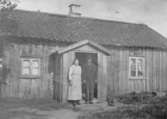 Lena Södergården. En äldre man och en äldre kvinna står vid en stuga. Lena.
