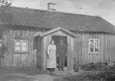 Lena Södergården. En äldre man och en äldre kvinna står vid en stuga. Lena.