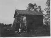 Bod tillhörande Johan Danielsson, Smedjekölen. Nössemark En flicka sitter vid boden. Fotots baksida är skrivet som ett vykort. Adresserat till fotografen Ragnar Blid, 1923.