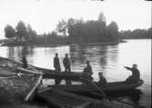 Män i två båtar i sjö med holme med monument på.