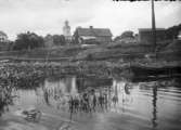 Sjö, gård, kyrka i bakgrunden.  Västmanland ?