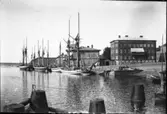 Skutor liggandes i G:a hamnkanalen. Närmast i bild ligger en galeas med sina typiska höga riggar lastad med virke. Längre bort syns även en s.k. älvbåt. Strömmerska huset till höger.
Foto fr. sent 1910-tal.