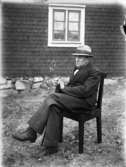 Porträtt av en äldre herre sittandes i stol utanför huset.