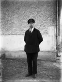 Man stående vid husvägg. På mössan står det MHF (Motorförarnas helnykterhetsförbund, grundat 1926).