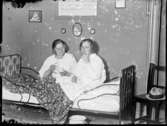 Två unga kvinnor sitter i sängen.
