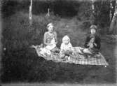 Tre barn på filt utomhus.