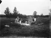 Fyra personer fikar utomhus på filt. Halle el. Hunneberg skymtar i bakgrunden.