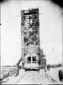 Arbete med järnvägsbron över nya trafikkanalen. I bruk från augusti 1916. På fotografiet ses sju manspersoner poserande uppe i bron. Till vänster ser man järnvägens banvall, vilken när bron stod klar muddrades bort.
Bron är ritad av en svensk, men konstruktionens upphovsman är Joseph Baermann Strauss, vilken ritat den något mer kända Golden Gate-bron i Kalifornien.
