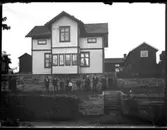 Olof Jonssons text: Samuelssons i Strömslund. Enligt församlingsboken 1920 så bodde här 18 personer 1920. Bland andra Slaktare Johan Alfred Samuelsson, Vassenda-Naglum 1859, hans hustru Amalia Kristina Samuelsson, Vassenda-Naglum 1862, deras barn: Diversearbetare Gustav Evald, Hjärtum 1893, Elektriker Ernst Algot, Vassenda-Naglum 1899, Yngve Ivar Samuel, Vassenda-Naglum 1903, och oä Karl Olof Fredrik, 1912. Gissningsvis så har vi slaktare Johan Alfred Samuelsson och hans fru stående till höger på bilden. Övriga troligen deras barn med familjer.