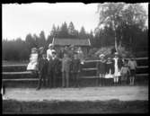 På bilden finns totalt 16 barn som sitter eller hänger på en inhängnad av träslanor. Längst till vänster sitter Elin Hansson, Gärdhem 1904-03-05 och som nummer tre sitter Alma Hansson, Gärdhem 1896-12-09. Övriga okända