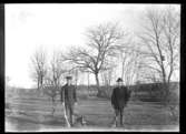 Abraham Jonsson, Hjärtum 1875-01-13, Johan Jonsson, Hjärtum 1880-11-01 stående med gevär och hund i trädgården på Torpet (Arnstorp) med Öresjö i bakgrunden
