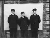 Abraham Jonsson, Hjärtum 1875-01-13,  Karl Johansson, Hjärtum 1888-05-14, Olof Jonsson, Hjärtum 1882-11-15, poserar framför vit duk som är uppsatt på väggen till det gamla boningshuset på Arnstorp.