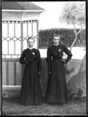 Gerda Johansson, Hjärtum 1893-10-15, och Märtha Bjurströms som konfirmander poserar framför målad bakgrund.
