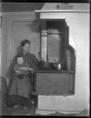 Olga, född Olsson, Forshälla 1891-05-12 med sonen Sven, Hjärtum 1915-05-14, sittande framför järnspisen med spiskupa i köket på Torpängen med hunden Sonja vid fötterna.
