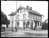 På trappan till Arvid Petterssons Diversehande och Speceriaffär står troligen några ur personalen. Enligt församlingsboken så bodde i huset 1910 15 personer. (Någon Arvid Pettersson finns inte angiven 1900, 1910 eller 1920.) Däremot finns angivet att 1910 så bodde i huset Chefsbiträde Maria Ahlström, Ale Skövde 1888, ev. kan detta vara damen med vitt förkläde. Övriga okända.