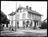 På trappan till Arvid Petterssons Diversehande och Speceriaffär står troligen några ur personalen. Enligt församlingsboken så bodde i huset 1910 15 personer. (Någon Arvid Pettersson finns inte angiven 1900, 1910 eller 1920.) Däremot finns angivet att 1910 så bodde i huset Chefsbiträde Maria Ahlström, Ale Skövde 1888, ev. kan detta vara damen med vitt förkläde. Övriga okända.