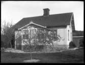 Wilhelm Ljunggrens boningshus med utsmyckad veranda och blommande aplar i trädgården.