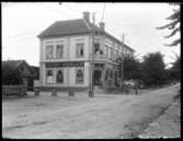 Olof Jonssons text: Charls Anderssons och Gustaf Svenssons hus i Strömslund. 1910 så bodde här 15 personer bl a Handlande Gustaf Adolf Svensson, Väne-Ryr 1881, hans hustru Linnea Ekman, Stora Tuna 1887 och deras dotter Birgit Linnea, Vassända-Naglum 1910. Gissningsvis kan det vara herr och fru Svensson som står på balkongen ovanför affären - som ägare till fastigheten borde de ju bo i lägenheten med balkong.