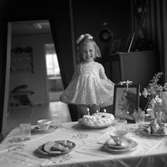 Lilla fröken Hellström på Västra Holmgatan 11 i Jönköping, fyller tre år. I finklänning och med rosett i håret står hon bakom det dukade kaffebordet. Bland koppar och fat finns kakor och en tårta med tre ljus i.