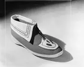 En toffla i vit och grå filt med vit krage, broderier och blixtlås.