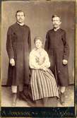 En kvinna sitter, och två män står bakom, klädda i folkdräkter