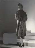 Nordiska Kompaniet. Kvinna i mörk minkpäls och hatt. Text på baksidan: 