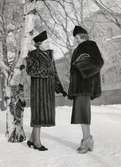 Nordiska Kompaniet. Två kvinnor poserar i en snöig park. Den ena bär en pälskappa, den andra en pälsjacka.