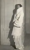 Nordiska Kompaniet. Kvinna i vit aftonklänning och vit pälskappa av hermelin. Hög, bred krage. Text på baksidan: 
