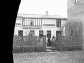 Mathilda Ranchs fotoateljé. Huset låg utmed Prästgatan, kv Bagaren, Varberg. Damen i grinden är Mathilda Ranch. (Glasplåten skadad i vänster sida)