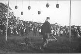 Midsommarfirande i den torrlagda vallgraven vid Varbergs fästning 1904. Tävlingar och lekar uppvisades av militärer från Volontärskolan. Åskådarna betraktar en deltagare i leken 