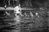 Några personer badar i Tulebosjön, 1930-tal. Det är antingen familjen Alberts eller sommargäster. I bakgrunden till höger ses en strand och träd.