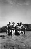 Fyra personer sitter på en sten ute i vattnet, troligtvis i Tulebosjön cirka 1930.
