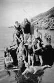 Badklädda personer poserar ståendes på något i vattnet, eventuellt vid Stenungsön, cirka 1930. Relaterade motiv: 2007_0287 - 0319.