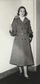 Nordiska Kompaniet. Tonårsmode 1950. Flicka i grå, utsvängd kappa med dubbla knapprader och knappar vid fickorna. Krage med skinn. Ljus halsduk. Text på baksidan: 