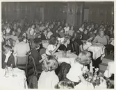 Nordiska Kompaniet. Tonårsmode 1950. Interiör med ung modepublik vid dukade bord med läskedrycksflaskor. Text på baksidan: 