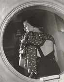 Nordiska Kompaniet. Kvinna i mörk aftonklänning med bar rygg. Kring axelpartiet ett arrangemang med en mörk schal med ljusa prickar. Text på baksidan: 