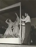 Tonårsmodevisning i Kungsträdgården i Stockholm, Nordiska Kompaniet. Tre kvinnor i mönstrade klänningar och man i vit skjorta, hatt med hakband och mörka byxor.