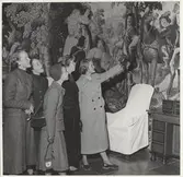 En grupp unga tjejer i kavajer, kjolar och kappor, tittar på väggmålning på Drottningholm Slott.