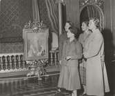 Fyra unga tjejer på Drottningholm Slott klädda i dräkt och kappa vid en målning.