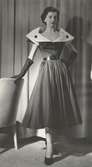 Modell i klänning med skärp och vit krage med stora knappar, handskar och pumps. Från Maggie Rouff.