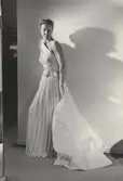 Modell i aftonklänning med släp och rosetter. NK:s Franska efter Madame Grès.