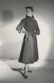 Modell i gråsvart kappa i ylle, grovt räfflad med nertsbesats, hatt och handskar. Från Manguin.
