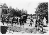 Sommardag vid sekelskifte på bron över till Vargön. Mannen längst till höger är disonent Carl Stenholm (vd 1899-1914 vid Wargöns AB). I bakgrunden skymtar den elktr transportbanan med sitt lilla tåg. vagnanarna lastade med slipmassa (Se Wargöns AB 1874-1949 sid 79).