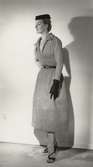 Modell i klänning med skärp, hatt och handskar. NK:s Franska, original J. Fath.